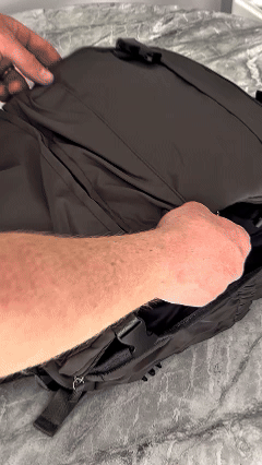 A traveler packing clothes inside a compression backpack