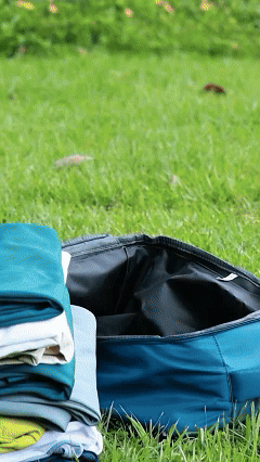 A traveler packing clothes into a blue travel backpack outdoors